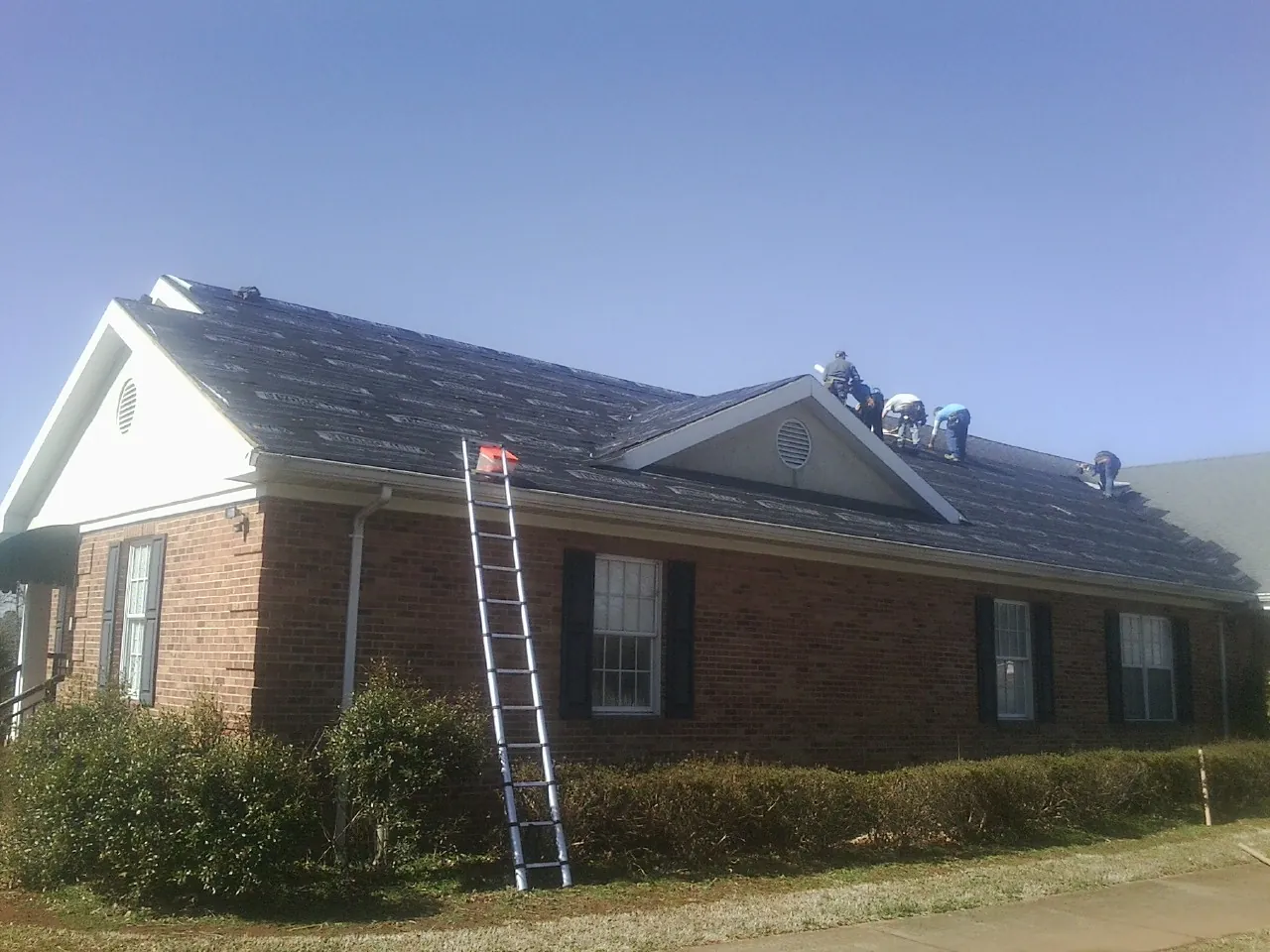 Crew tearing shingles off a brick ranch roof with a ladder set — Emergency Roof Repair work by our crew in Ephrata
