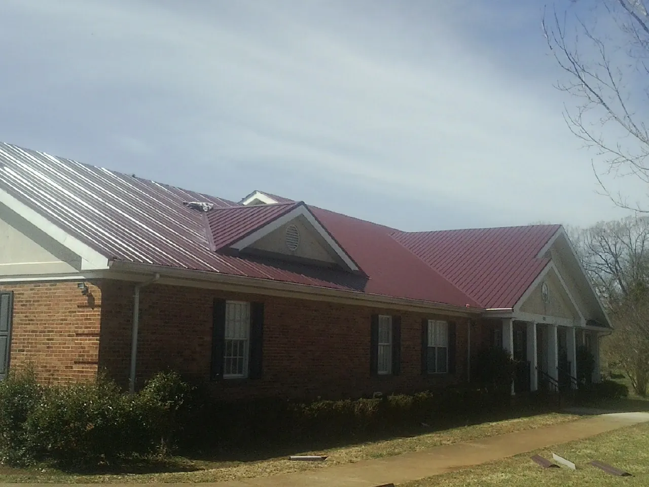Red metal roof with gabled entries on a long brick building, from a Hail Damage Roof Repair job in Ephrata