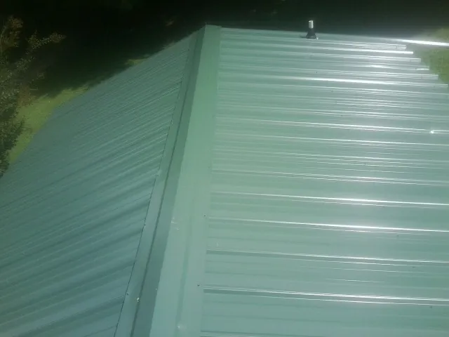 New green metal panels meeting at the ridge of a roof — Flat Roof Repair work by our crew in Ephrata