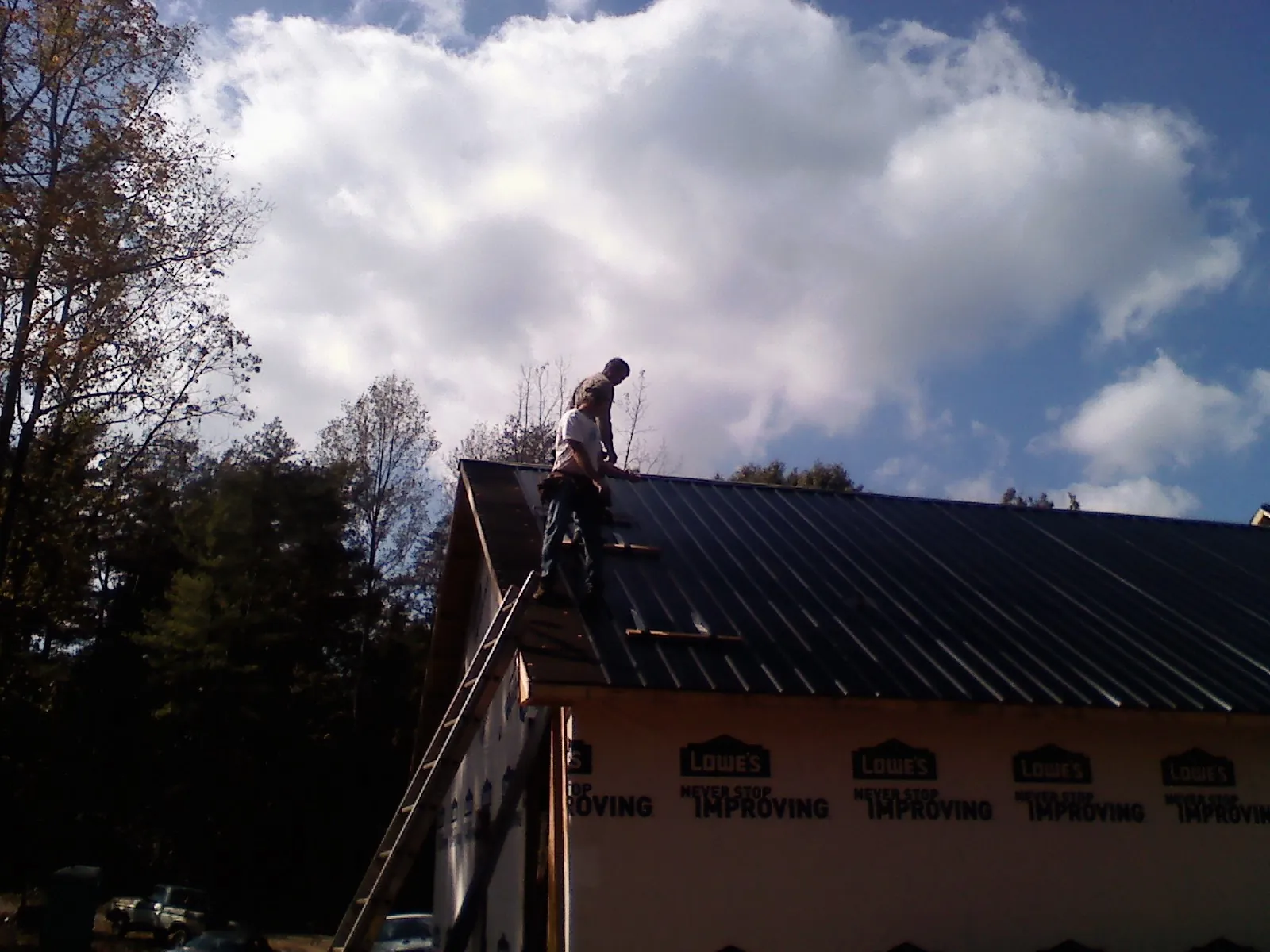 Roofer fastening dark metal panels high against a cloudy sky, from a Roof Inspection job in Ephrata